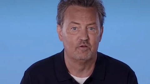 Image of Actor Matthew Perry wearing a black shirt in front of a light blue background.
