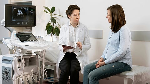 An image of doctor and a pregnant woman sit in a clinic, discusses with the woman near an ultrasound machine.