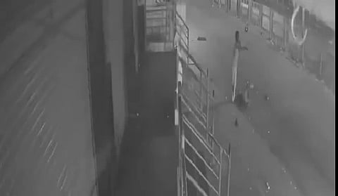 A video footage screenshot where a silhouette of a woman is seen pleading on a road with someone lying down at her feet.