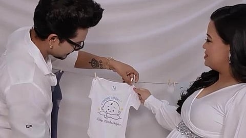 A couple in white clothes holding a newborn dress at their baby shower.