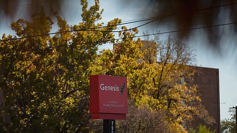 An image of red sign for Genesis Uptown Rehabilitation Center stands against autumn trees and a building.
