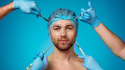 An image of a man with surgical markings on face, wearing a hair cap. Gloved hands holding scalpels and syringe surround him.