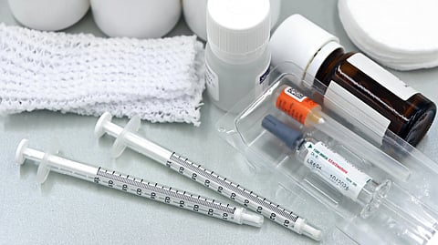 An image of medical supplies including syringes, vials, and bottles are arranged on a table.
