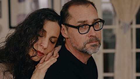 A woman rests her head gently on a man's shoulder.