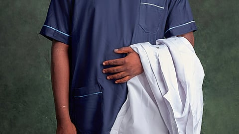 Close-up of a nurse wearing dark blue scrubs and holding a white apron.