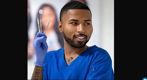 Brandon Dillard in blue scrubs and holding dental instruments in his right hand.