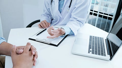 A doctor in a white coat consults with a patient across a desk.