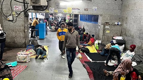 Crowded shelter with people resting on blankets across the floor.