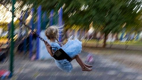 A young girl in a blue dress joyfully swings in a park.