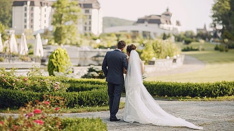 Bride and groom walk arm in arm through a picturesque garden.