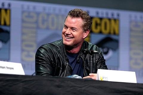 Eric Dane at a press conference wearing a black a jacket and a navy-blue t-shirt.