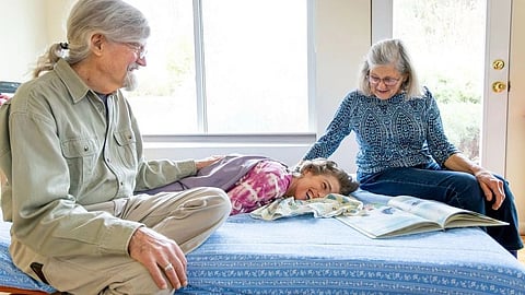 An older woman sits on a bed with a girl and a man.