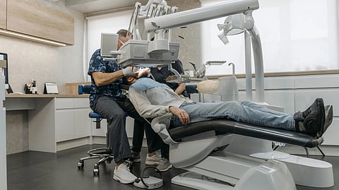 A dentist wearing a floral shirt examines a patient lying back in a dental chair.