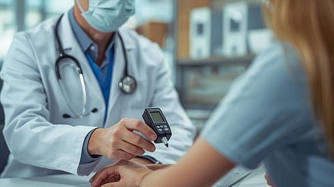 A doctor in a mask uses a glucose meter on a patient's hand in a clinical setting.
