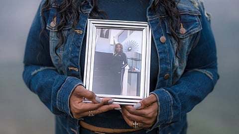 A person in a denim jacket holds a framed photo of a woman in sportswear.