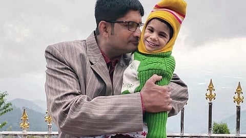 A man in a striped suit lovingly embraces a child in a green sweater and colorful hat, both smiling.