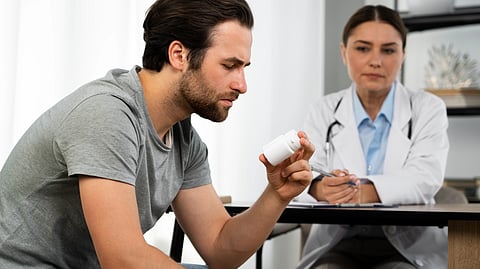 A man looks at a medicine bottle while a doctor watches him.