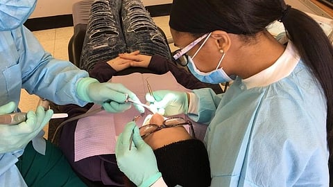 Two dentists in blue scrubs and masks perform a dental procedure on a patient lying in a chair.