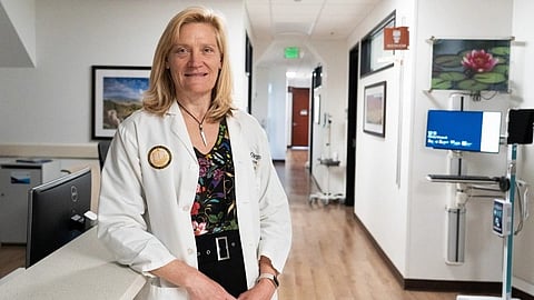 A woman in a white coat stands confidently in a hospital hallway.