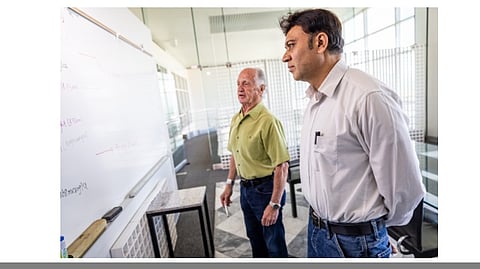 2 men standing next to each other and board in front.