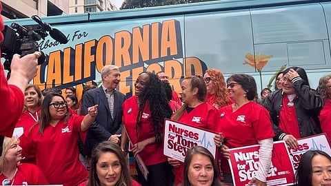 A group of nurses in red shirts stand smiling in front of a bus with "California" text.