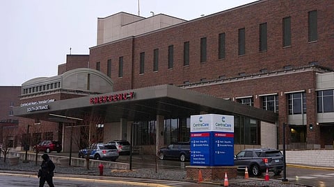 A hospital building with an emergency entrance, parked cars, and a person walking nearby.