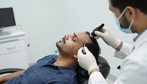 Indian man sitting in modern clinic chair, specialist performing microscopic scalp treatment for hair loss