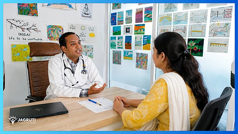 A doctor consults a female patient across a desk in a clinic.
