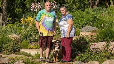 A man, woman, and dog stand in a garden.