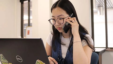 A woman with glasses works on a laptop while talking on the phone.