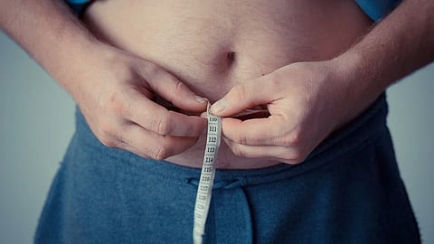 A person measures their waist with a tape measure, focusing on health and body monitoring.