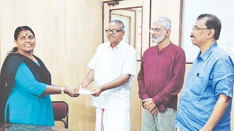 ഷൈലജ ബാലൻ ബാങ്കിലേക്ക് തുക കൈമാറുന്നു