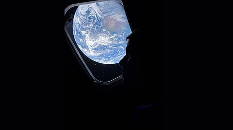 Astronaut Reed Wiseman looks out the Orion window at distant Earth during the Artemis II mission.