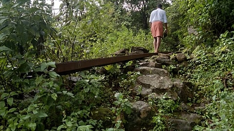 A resident of Veerankudy tribal colony walks over an iron post used as bridge over a trench on his way home