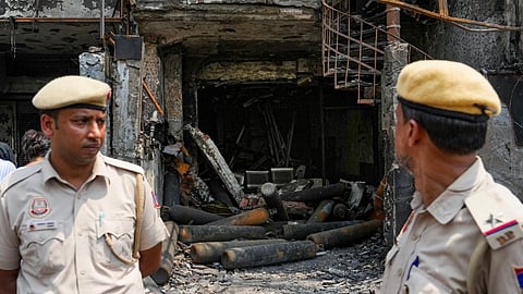 Police personnel stand in the backdrop of burnt oxygen cylinders at the site of the fire at the Baby Care Hospital, at Vivek Vihar, in East Delhi, Monday, May 27, 2024.