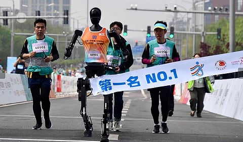Robotic participant "Tiangong Ultra" (2nd L) crosses the finish line as engineers run alongside during the Beijing E-Town half-marathon and humanoid robots half-marathon. April 19, 2025.