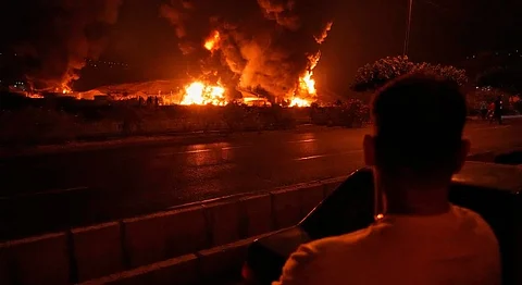 A man looks at flames rising from an oil storage facility after it appeared to have been struck by an Israeli strike in Tehran, Iran, early Sunday, June 15, 2025.
