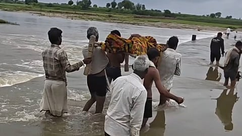 Villagers Carry Pregnant Woman on a Cot Across a Flooded Culvert in Morena