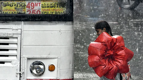 A woman folds her umbrella before entering an RTC bus amidst light rains on Monday in Hyderabad