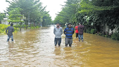 Residents of La Polama Villas in Mokila, Rangareddy district, wade through floodwaters on Monday
