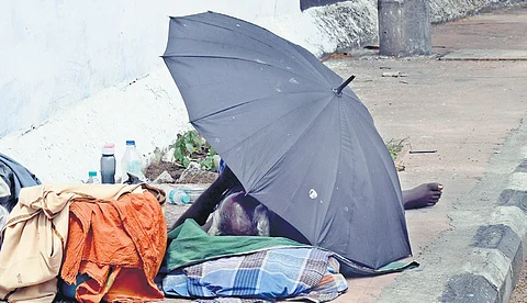 An elderly homeless person resting on a footpath under the shade of umbrella at Royapuram.