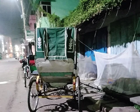 A homeless rickshaw-puller sleeping under mosquito net in front of a closed shop at Dolamundai