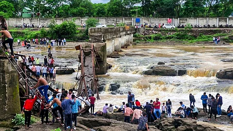 People stand near an iron bridge over the Indrayani river after it collapsed, in Pune district, Maharashtra, Sunday, June 15, 2025. Some people are feared to have been swept away after the collapse.