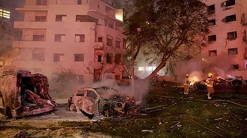 A firefighter holds a hose near charred vehicles in the Israeli city of Tel Aviv after a fresh barrage of Iranian rockets on June 16, 2025.