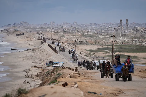 Displaced Palestinians, carrying their belongings move between southern and northern Gaza along a beach road, in the outskirts of Gaza City, on March 21, 2025.