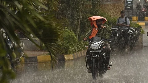 A man is covering himself from the rain while riding his bike at Somajiguda in Hyderabad.