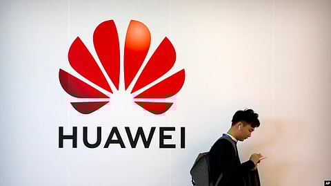 A man uses his smartphone as he stands near a billboard for Chinese technology firm Huawei at the PT Expo in Beijing.