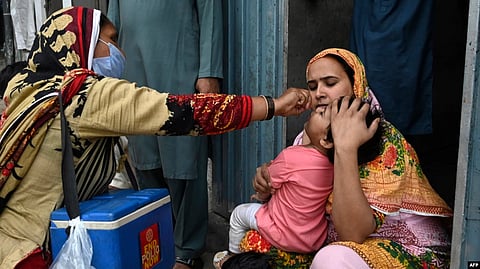A health worker administers polio vaccine drops to a child during a door-to-door polio vaccination campaign at a slum area in Lahore, Pakistan, May 23, 2022.