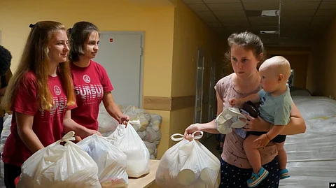 A woman carries her child as she receives humanitarian aid provided by local authorities in Selidovo, Donetsk region, Ukraine, Tuesday, June 14, 2022.