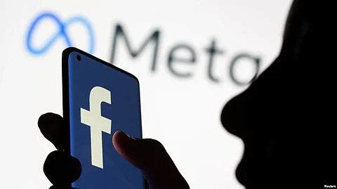 FILE - A woman holds a smartphone with the Facebook logo in front of a display of Facebook's new rebrand logo Meta in this illustration picture taken Oct. 28, 2021.
